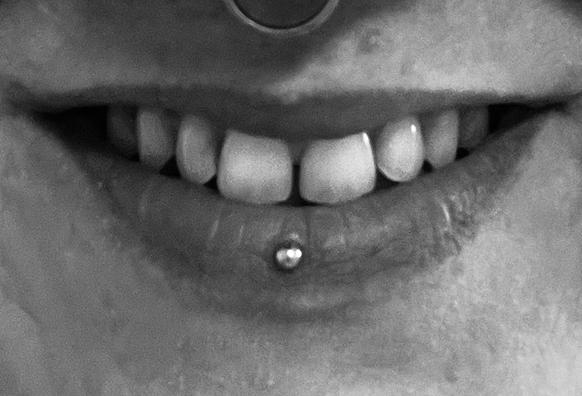 Lächeln der Userin, der Mund ist leicht geöffnet, man erkennt auf der Unterlippe ein Piercing und am oberen Bildrand sieht man einen Teil eines Ringes.