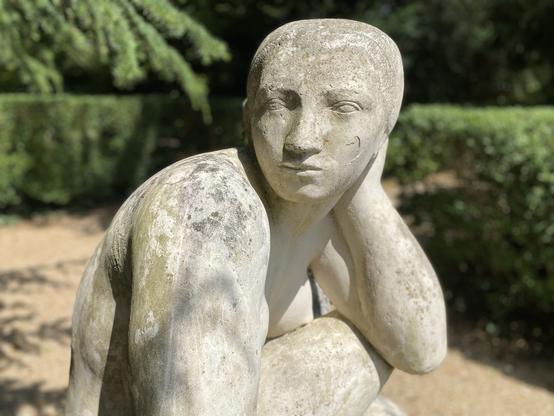 Statue en marbre. Une femme assise en tailleur se passe une main dans les cheveux