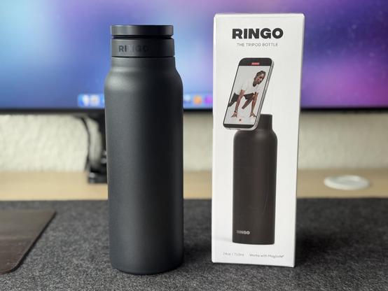 Schwarze Ringo Pro-Trinkflasche steht neben der Verpackung auf einer dunklen Filzmatte vor einem Mac-Bildschirm.