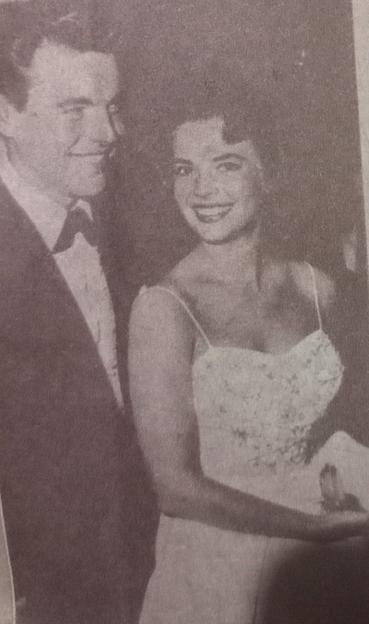 Una imagen en blanco y negro de Natalie Wood y Bob Wagner sonrientes en un evento, con la mujer usando un vestido sin mangas decorado con flores y el hombre vestido con un esmoquin.