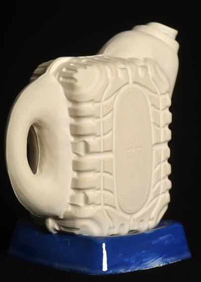 A slip casted ceramic pitcher that looks like pieces of plastic container put together. The main body part, the handle and spout are unglazed white stoneware, the base is a glossy blue upside down ceramic imitation of another plastic container.