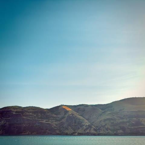 A shoreline of rolling hills in the distance stands under a bright blue sky on a sunny day.