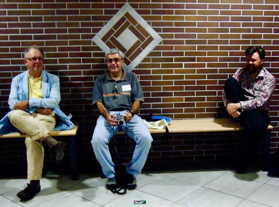 Three men, seated on a bench, in front of a brick wall.

From left to right, Albert Visser, in a blue jacket over yellow shirt and trousers, Aldo Antonelli, in a grey shirt and jeans, holding a camera, and to the right, Greg Restall, in a paisley shirt and dark jeans.
