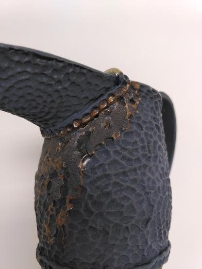 Handbuilt matte black ceramic pitcher with hammered like textured that are usually found on metallic object. some part look kind of rusty from a metallic glaze used on it.
Close-up on the part under the spout.