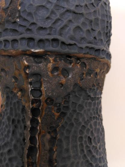 Handbuilt matte black ceramic pitcher with hammered like textured that are usually found on metallic object. some part look kind of rusty from a metallic glaze used on it.
Close-up on the part where it looks like soldered metal parts.