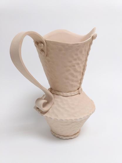 Bisque fired handbuilt pitcher. Handbuilt. It has a hammered like texture like we can find on hammered copper objects. it is built out of 3 conical parts. 2 cones are creating the body and the third creates a large spout opening. big flat handle.
