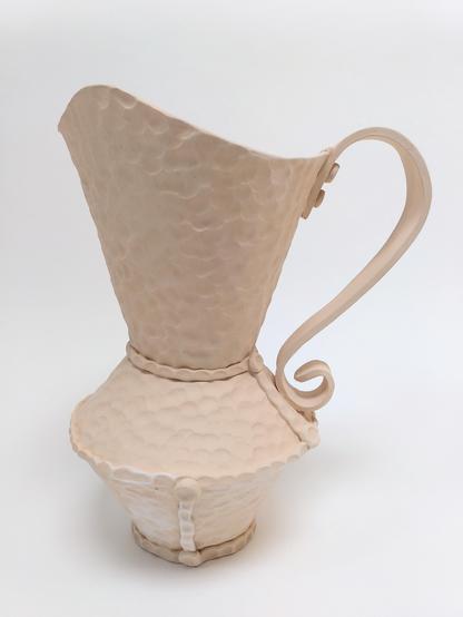 Bisque fired handbuilt pitcher. Handbuilt. It has a hammered like texture like we can find on hammered copper objects. it is built out of 3 conical parts. 2 cones are creating the body and the third creates a large spout opening. big flat handle.
