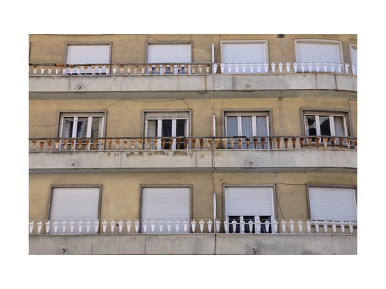 close up of a residential building with yellowish facade in a lisbon neighborhood. most shutters are down and parts of balcony railings are rusty and white.