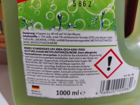 Das Bild zeigt die Rückseite einer Flasche Reinex Schmierseife mit einer grünen Etikett. Die Etikett enthält Informationen in deutscher Sprache. Oben auf der Etikett steht die Nummer "5862". Darunter ist die Dosierung aufgeführt: "4 Kappen (ca. 80 ml) auf 10 Liter Wasser." Die Inhaltsstoffe sind aufgelistet: "5-15% Seife, unter 5% nichtionische Tenside; EDTA und dessen Salze; Duftstoffe, LIMONEENE, CITRAL; enthält Konservierungsmittel, METHYLISOTHIAZOLINONE, NONE, BENZISOTHIAZOLINONE." Ein Warnhinweis in einem roten Warnsymbol mit einem Ausrufezeichen und der Aufschrift "ACHTUNG Enthält METHYLISOTHIAZOLINONE" ist ebenfalls vorhanden. Weitere Sicherheitshinweise und Anweisungen für Hautreaktionen, Augenschutz und Behandlung bei Kontakt mit Augen sind auf der Etikett zu finden. Die Flasche hat eine Kapazität von 1000 ml und ist von Reinex GmbH & Co. KG, Bladenhorster Str. 114, D-44575 Castrop-Rauxel, Deutschland hergestellt.