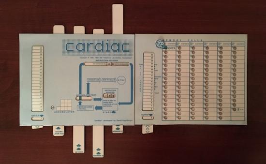 The image shows a vintage educational model of a cardiac computer, likely used for teaching the basics of computrers and computer programming. The model is laid out on a dark wooden surface, with two main components visible.

On the left side, there is a light blue card with the word "cardiac" prominently displayed at the top. Below the title, there is a flowchart with arrows and labels, indicating the process of the program. The flowchart includes terms like "accumulator," "test," and "setup," and features a series of vertical slots with numbered tabs, likely for inputting data. There are also several rectangular tabs at the bottom, each labeled with terms such as "accumulator" and "number."

On the right side, there is a beige card with a grid of circles, labeled "memory cells," arranged in columns and rows. Each circle can be marked, possibly to represent different computer memory locations. The top of this card has a section labeled "memory," with a column of circles and a vertical scale on the left, likely for recording time intervals.

The overall design of the model is educational, with clear labels and diagrams to facilitate learning about computer operations and programming.

Provided by @altbot, generated privately and locally using Ovis2-8B