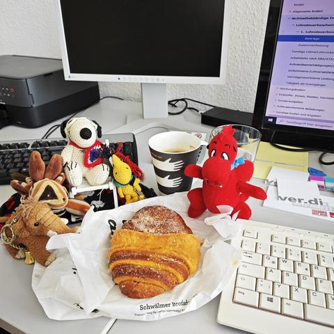Manni, Knelvis, Snoopy, Woodstock und Smok vor dem Rechner versammelt um ein Franzbrötchen. Zwischen Woodstock und Smok eine Verdi Sammeltasse mit weißen Händen auf schwarzem Hintergrund (auf der anderen Seite wird der schwarze Hintergrund zu Händen. Oben am Rand ein Zitat von Nelson Mandela.