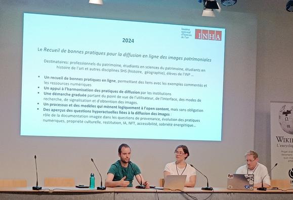 Photographie numérique couleur en format paysage.
2 hommes et une femme derrière une grande table sur une estrade, avec un écran présentant un texte sur le recueil des bonnes pratiques présenté par Damien Petermann.