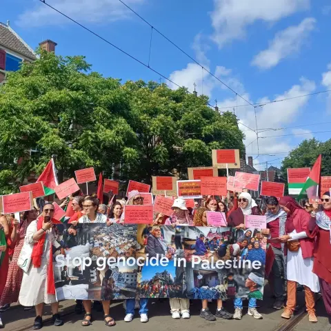 Mensen tijdens de demonstratie de Rode Lijn op 15 juni 2025 met een banner STOP GENOCIDE IN PALESTINE. Op het spandoek staan foto's van de genocide in Gaza.