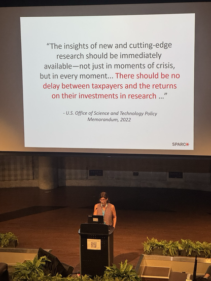 Heather Joseph giving a keynote with a slide in the background citing the U.S. Office of Science and Technology Policy: "The insights of new and cutting-edge research should be immediately available—not just in moments of crisis, but in every moment... There should be no delay between taxpayers and the returns on their investments in research ...“