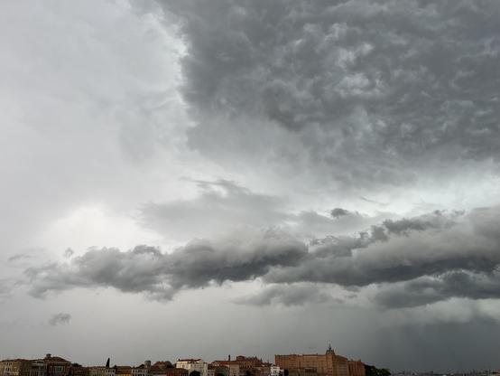 The rooftops of the island of Giudecca along the bottom of the frame. Above, roiling dark grey clouds in a pale grey sky, full of foreboding.