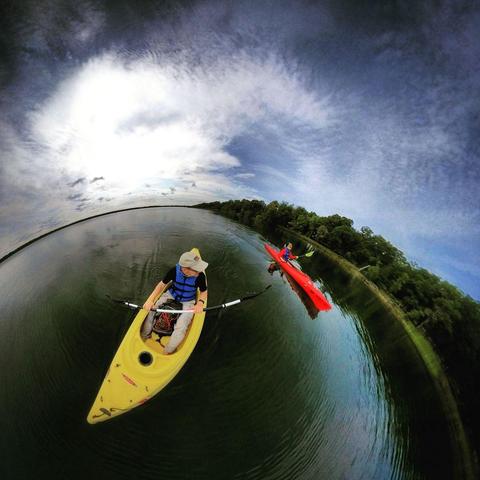 One of a series of photographs in which two people are pictured hiking, biking, and kayaking throughout a beautiful and verdant state park in central Minnesota under cloudy blue late-summer skies.