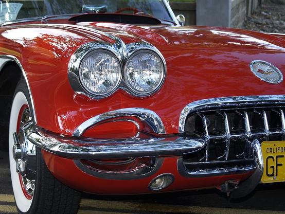 Little Red Corvette

This is a closeup photograph of a 1960 red Corvette.
The lower left of the image shows the white wall tire with chrome hubcaps. 
The chrome bumper runs a near vertical line across the bottom of the image leading to a bright, shiny, chrome grill. 
On the right side of the image you can see the circular Corvette badge on a shiny red hood.
Above the left fender are a pair of round headlights wrapped in chrome. There is also a chrome piece on the hood that leads back to the windshield.