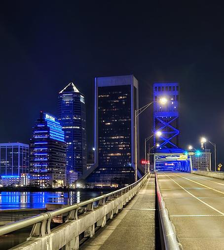 Late night view from pedestrian crossing on the iconic Main Street Bridge, with blue lighting over the river with the glowing downtown skyline ahead.