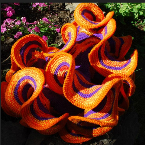 A picture of hyperbolic crochet. It's a fabric object that looks like a frilly flower, almost like something you'd see at the bottom of the ocean, and each one has a stripe pattern of orange, yellow, and blue. It's really quite impressive.