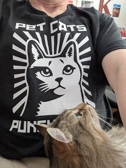 Me wearing my new t-shirt, which has a bold graphic of a cat and the words "PET CATS; PUNCH NAZIS" with my cat Phasma on my lap looking up.