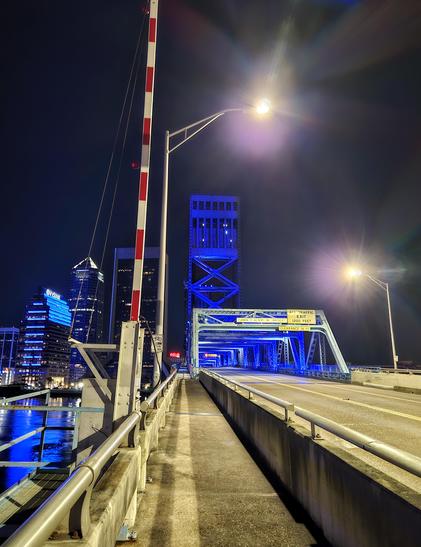 Late night view from pedestrian crossing on the iconic Main Street Bridge, with blue lighting over the river with the glowing downtown skyline ahead.