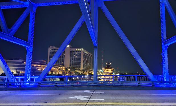 From pedestrian crossing, late night, looking upwards into the huge metal bridge structure, glowing from blue night lighting.