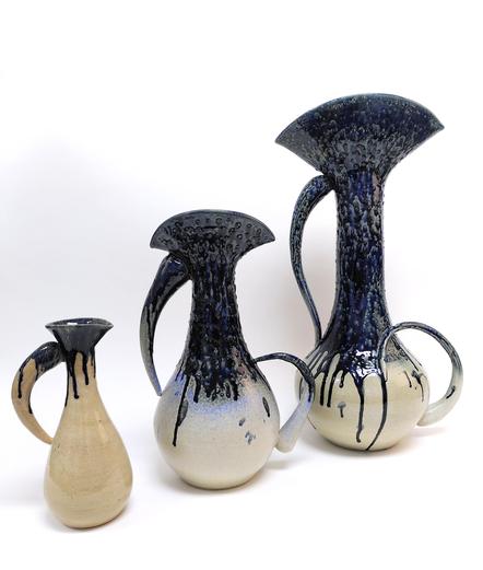 Triptych of ceramic pitchers. Inspired by water drops. 3 pitchers of different sizes. Their body is like a water drop shape. Handles are elongated water drops. White or clear glaze on the bottom part. Blue drippy glaze like water overflowed on the top half part.