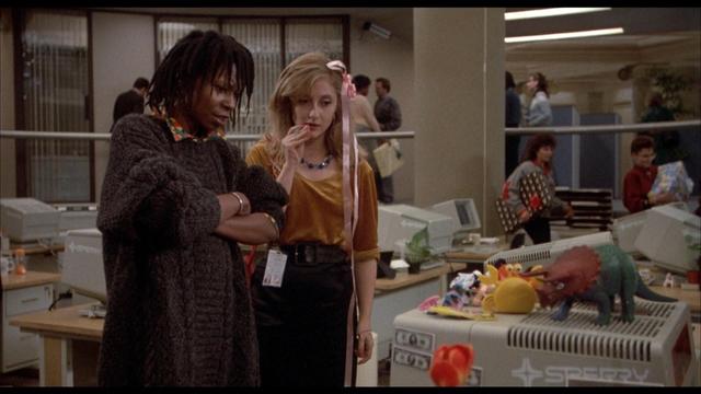 Whoopi Goldberg and Carol Kane looking skeptically at a computer in an open plan office.