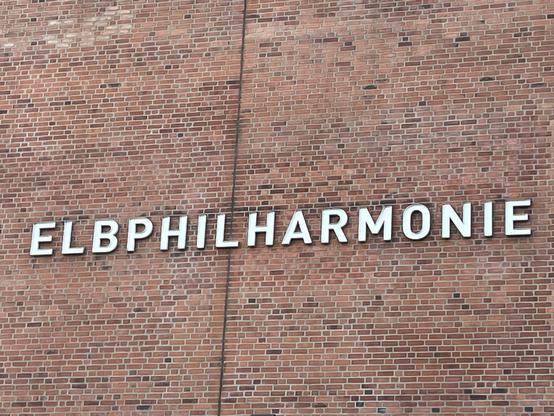 The image shows the word "ELBPHILHARMONIE" displayed on a brick wall, indicating the Elbphilharmonie concert hall in Hamburg, Germany.