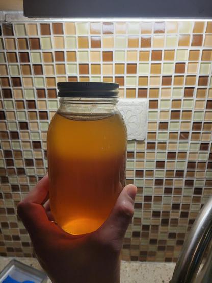 A jar of honey held up to the light. the bottom is a medium amber color, but there is a relatively sharp dividing line about 2/3 of the way up and the top honey is a light tan.