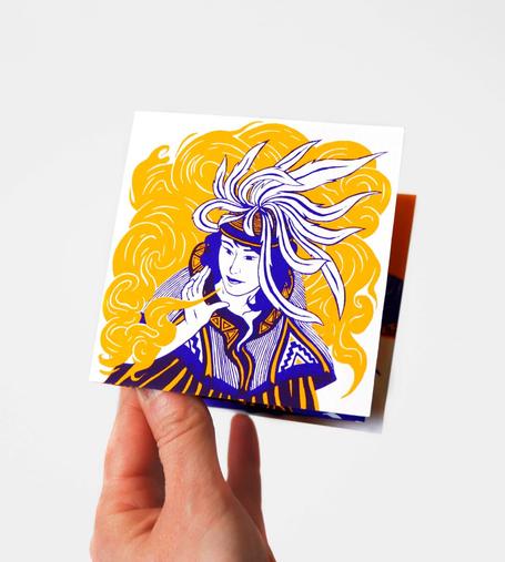 This photo shows a hand holding a small leporello printed in screen printing. On the cover, a two-color illustration in yellow and purple depicts a woman wearing a headdress made of long, flowing feathers. Her face is turned to the left. She holds her hand up and blows into it, releasing an orange smoke from her fingers. Her clothing is decorated with graphic patterns reminiscent of embroidered fabric. The edition is photographed against a white background. This leporello is part of a silkscreen-printed series, available on my online shop.