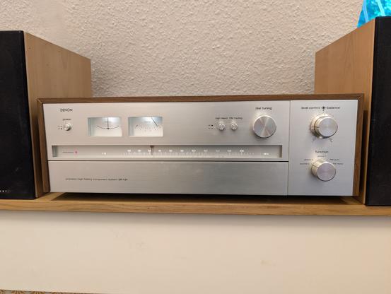 A huge receiver with a silver front, an FM scale and three big knobs for tuning, volume and input select. To the left there are two instruments showing signal strength and tubing. It looks very elegant and minimalist.