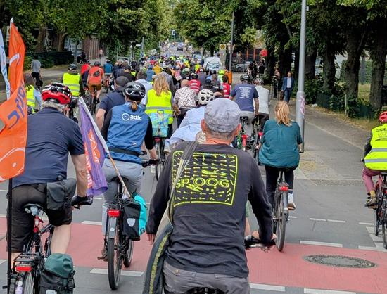 Eine große Fahrraddemonstration fährt eine Straße entlang. Ganz links flattert eine orangene adfc-Fahne.