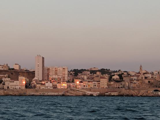Le quartier d'Endoume au soleil couchant, vu depuis la mer. On voit des vitres qui brillent du reflet orange feu du soleil couchant.