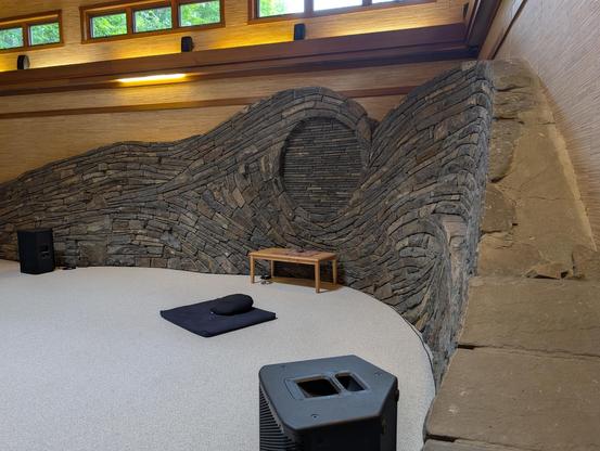 Interior of the Omega Center sanctuary, with a curved rock wall with swirls in it, looking almost like a dragon head, against a beige carpet floor and a warm wooden wall, with small windows above.