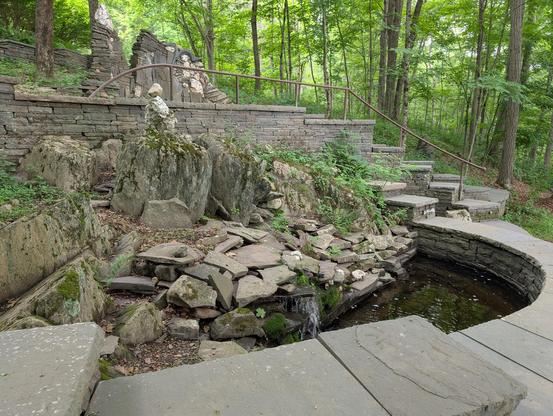 Stonework surrounding a small pond, with greenery growing out of the stonework.