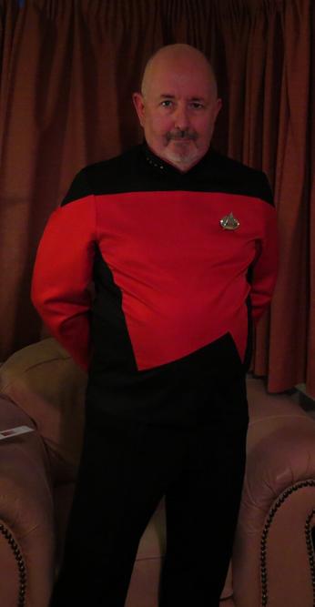 Chris in his living room, dressed in a "Star Trek: The Next Generation" era command uniform with four pips on the collar, because of course he is.