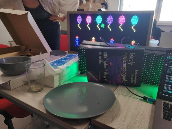 A bright LED matrix display showing colorful balloons and stick figures in party hats