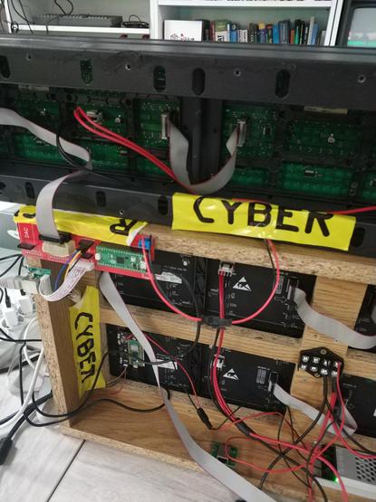 Back panel of DIY LED matrix display cases, with various cables hanging out and devices tacked on with yellow tape that says "CYBER"