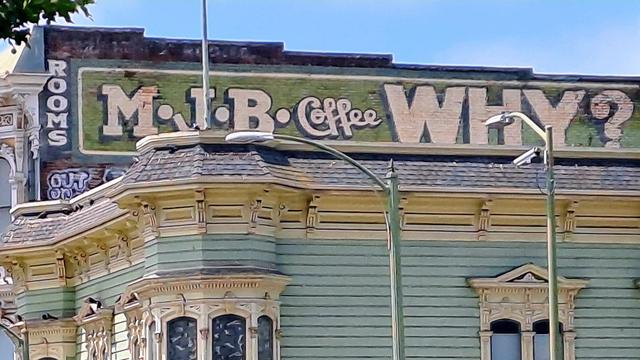 Sign painted on a horizontal strip across the top most portion of a building advertising "Rooms" and "M.J.B. Coffee, Why?"