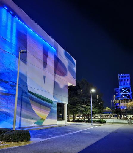 Late night view of the side to the city Chamber of Commerce building with a colorful mural, glowing from blue neon lighting, and in the background, the iconic Main Street Bridge also illuminated in blue lighting.