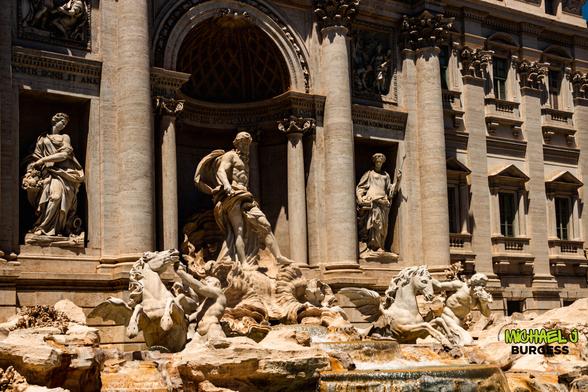Daytime close-up of Trevi Fountain in Rome showing central statue of Oceanus flanked by two figures in niches, marble horses rearing in the foreground, and water cascading over sculpted rock into the basin below.