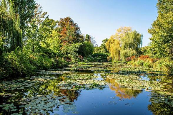 A serene view of the water lily pond at Monet's Garden in Giverny, France, showcasing vibrant greenery and reflections, embodying the essence of Impressionist art.