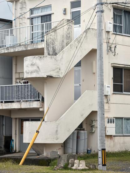A staircase of a small housing building. The painting is white, but old looking with parts of the paint peeling in places.