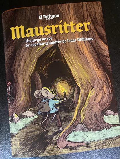 Portada del juego de rol Mausritter. En ella un valiente ratoncito vestido con pantalones marrones, jubón azul y una mochila de cuero a la espalda se adentra en una oscura cueva mientras se ilumina con una antorcha que sujeta en su mano derecha.
