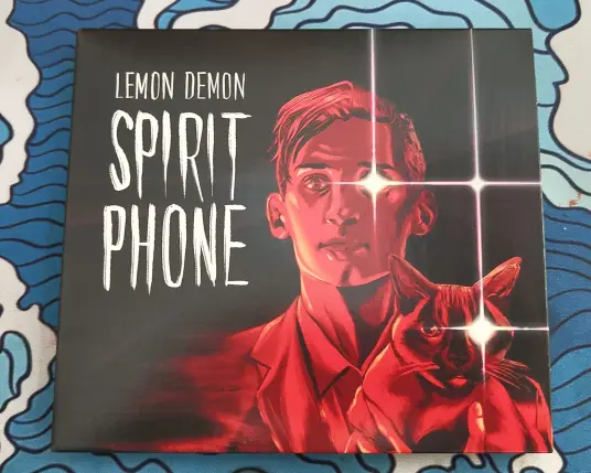 Cover of Lemon Demon's Spirit Phone.  Artist name and album title along with red art of Neil Cicierega and a cat with glowing right eyes.