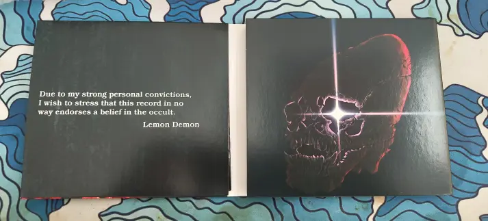 Inside the first fold of the album, with a quote on the left side and art of a cone headed skull with a glowing right eye.

"Due to my strong personal convictions, I wish to stress that this record in no way endorses a belief in the occult.  Lemon Demon"