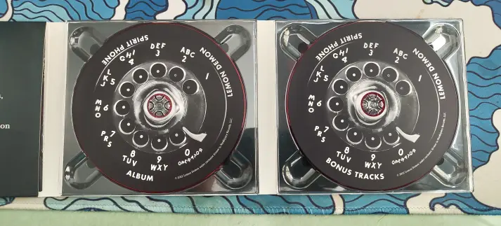 Two discs with rotary phone dial designs, one labeled "Album", the other "Bonus Tracks".  Both are labeled with the band name and album title.