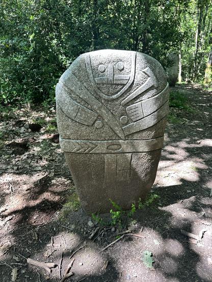 Reproduction of a 3000 year old granite menhir in the hills of Occitane. Simplified face with maybe tattoos, arms, axe. Original is fragile & protected. Many of these were either androgynous or had their gender signifiers changed over centuries. This one has both male and female characteristics.