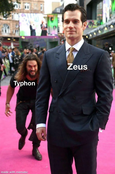 Photograph showing Henry Cavill on a red carpet with Jason Momoa sneaking up on him in the background in a silly manner. Henry, in the foreground, is labeled "Zeus," while Jason, in the background, is labeled "Typhon."